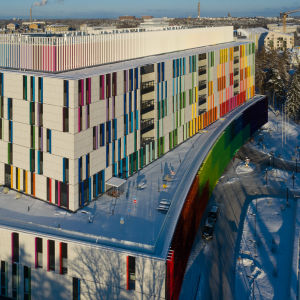 Uusi lastensairaala Helsingissä ilmasta kuvattuna. On talvi, maassa on lunta ja aurinko paistaa kirkkaasti. Lastensairaalan seinässä on paljon eri värejä. 