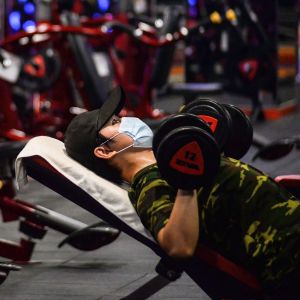 En man i munskydd lyfter vikter på ett gym.