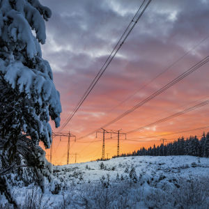 A sunset on a snowy landscape with power lines. 