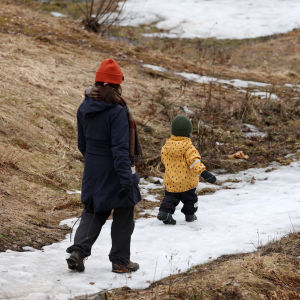 Aikuinen ja lapsi kävelevät lumista kävelytietä pitkin, vieressä näkyy sulaa maata.