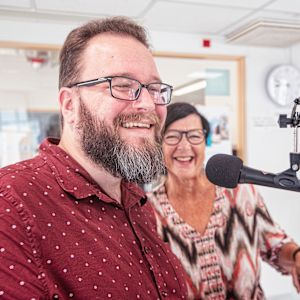 Kuvassa mies ja nainen radiostudiossa. He hymyilevät radiolähetystä tehdessään.