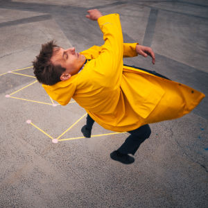 Matemaatikko Juhani Koivisto hyppää keltaisessa sadetakissa. Maahan on piirretty liidulla matemaattinen kuvio. 