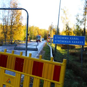 Bron över Strömma kanal vid Kimitoön är avstängd och avspärrad. På bilden syns flera olika väghinder och en lastbil mitt på bron. Träden är höstgula. På bilden syns också en trafiksskylt med texten Strömma kanal.