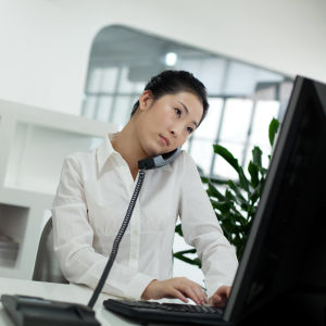 En kvinna talar i telefon medan hon jobbar framför en dator.