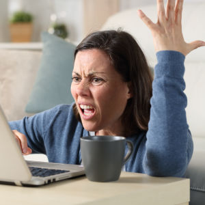 Kuvassa on nainen toinen käsi ylhäällä ja toinen kannettavan tietokoneen näppäimistöllä. Hän näyttää nähän yllättyneeltä ja ärtyneeltä. 