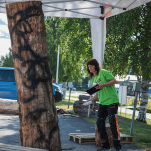 Ulla Haglund använder sig av sprayfärg för att gestalta proportioner. Etualalla puupölli, johon maalattu mustalla spraymaalilla kuvioita, taustalla nainen maalipurkki kädessä, katsoo pölliä