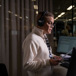Kuvassa selkouutisten juontaja Tuukka Lukinmaa seisoo tietokonenäyttöjen edessä ja lukee paperilta selkouutisia radioon.