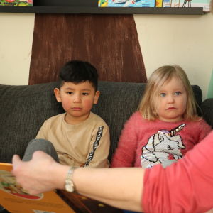 Två barn lyssnar på en småbarnspedagog som läser saga.