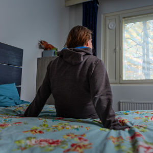 Nainen istuu sängyllä selin kameraan.