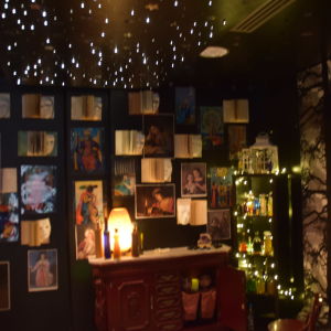 Ett mörkt rum med böcker och affischer på väggarna. Stämningsbelysning i form av ljusgirlanger. Bibliotek, sagorum.