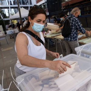 En kvinna med munskydd lägger sin röstsedel i en valurna.