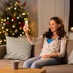 Leende kvinna sitter i en soffa och ser på sin telefon, i bakgrunden en julgran