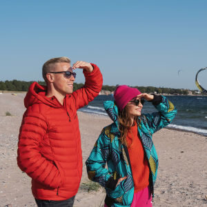 Egenandin juontajat Nicke Aldén ja Hannamari Hoikkala katselevat aurinkoisena päivänä Tulliniemen rannan purje- ja leijalautailijoita.
