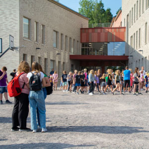Barn och unga står i klungor utanför skolbyggnad.