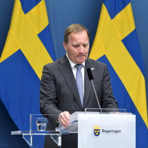 Stefan Löfven framför två svenska flaggor.