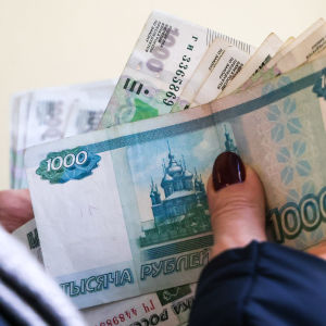 Nippu automaatista nostettuja ruplan seteleitä naisen kädessä. Päällimmäisenä tuhannen ruplan seteli.
