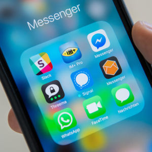 En ruta med olika appar (bland annat Whatsapp och Signal) på en telefonskärm. En hand håller i telefonen.