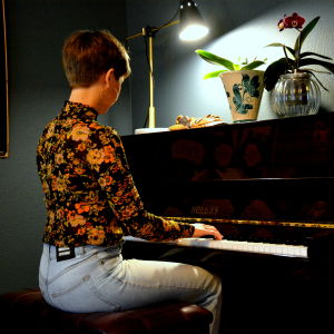 en kvinna i blommig tröja och jeans sitter och spelar piano