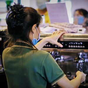 En kvinna står med ryggen mot kameran och lagar kaffe i ett kafé. 