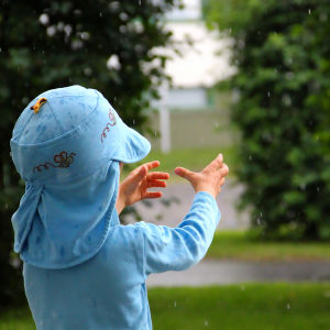 Ett litet barn fösöker fånga regnet med händerna.