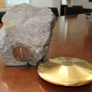 Kuvassa on pöydällä kultainen kiekko, jonka vieressä koristekivi, jossa on kiinni metallinen sotainvalidien veljesliiton tunnuslaatta.