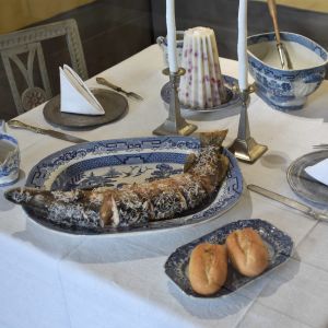 Bord i 1700-talsstil dukat i blå-vitt porslin med en ugnsstekt gädda och två semlor.
