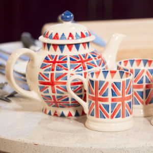 En tekanna och muggar dekorerade med brittiska flaggan står på ett bord.