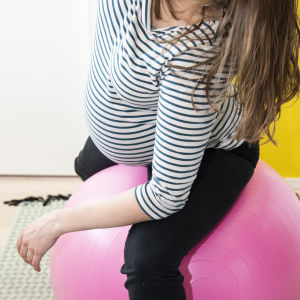 Raskaana oleva nainen venyttelee jumppapallon päällä.