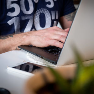 Lähikuva: mies kirjoittaa kannettavalla tietokoneella.