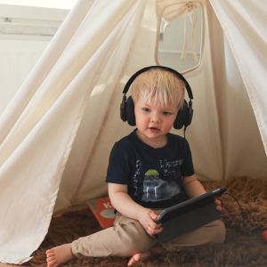 Pieni lapsi kuulokkeet korvilla kuuntelee ohjelmia älylaitteelta.