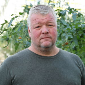 En man med kort grått hår står inne i växthus.
