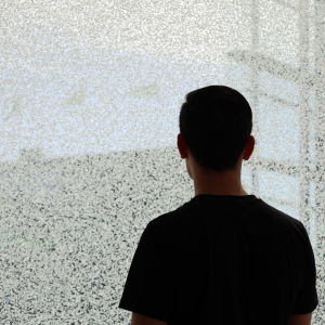 En ung man framför en glasvägg tittar ut. 