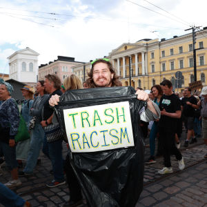 Mielenosoittaja Paul Nix esittelee roskasäkkiä, jossa lukee "TRASH RACISM". Taustalla on mielenosoituskulkue.