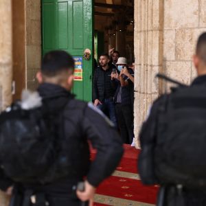 Palestinier tittar ut genom dörren i al-Aqsamoskén i Jerusalem, israelisk polis bevakar byggnaden.