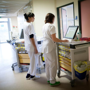 Två sjukskötare fotograferade bakifrån i en sjukhuskorridor.