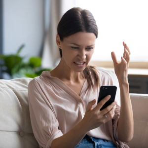 Irriterad ung kvinna sitter i en soffa och tittar på sin telefon