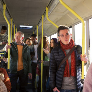 Människor i olika åldrar står och sitter i en buss.