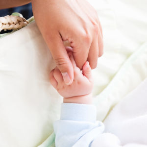 Kvinnohand håller i en babyhand vid en babysäng.
