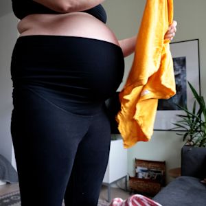 Raskaana oleva henkilö asettelee vaatteita.