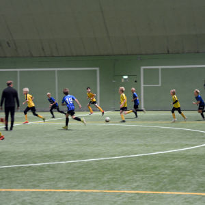 Fotbollsspelare från åifk p11-laget och FC Inter spelar fotboll på en fotbollsplan inomhus.