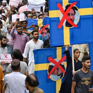 Mielenosoitus, jossa ihmiset marssivat ruotsin lippujen kanssa, joissa kuva Salwan Momikan kasvoista ja niiden päällä punainen ruksi.