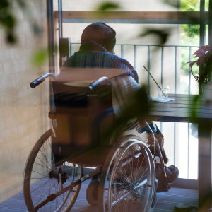 Pyörätuolissa istuva ihminen katselee ulos parvekkeelta.