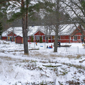Ett rött hus skymtar bakom träd. Det är snö på gården och någrab arn åker pulka. Det är Österbo daghem.