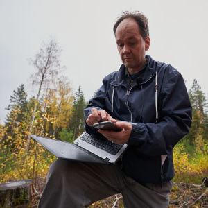Jari Natunen näppäilee kännykkäänsä maastossa.