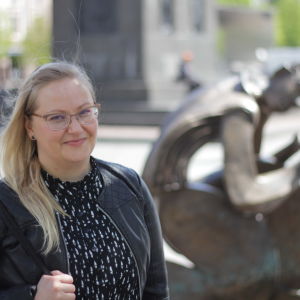 Vit kvinna med långt blont hår står framför en skulptur av Erikki Kannosto.