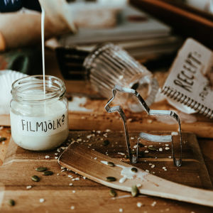 Ett smutsigt köksbord med en öppen receptbok, en pepparkaksform och en glasburk som fylls av en vit vätska. På burken står det "filmjölk" med frågetecken.