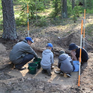 En man och tre barn gräver efter arkeologiska fynd i skogen.