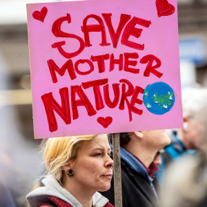 En blond kvinna med piercingar demonstrerar och håller i en rosa skylt där det står "rädda moder jord".