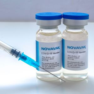 Två doser av Novavax-coronavaccinet på ett bord. Bredvid doserna en spruta.