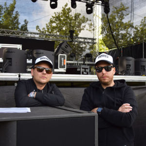 Två personer med solglasögon står framför en scen.